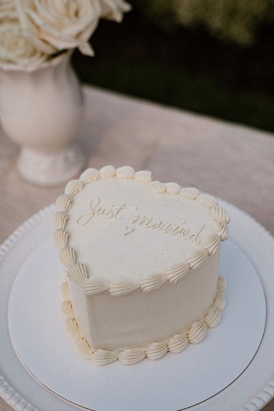 a white heart-shaped wedding cake with calligraphy and some vintage-inspired decor is a cool idea