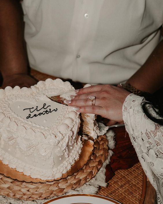 a white heart-shaped wedding cake with sugar details and some black calligraphy on top is a cool idea for a modern or vintage wedding