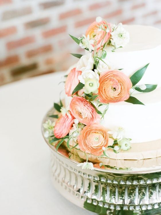 a white wedding cake with peachy pink and orange blooms and white ones plus greenery for a refined wedding