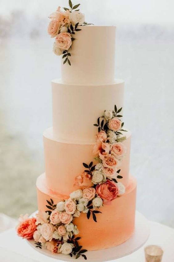 an ombre white to peach wedding cake decorated with white, blush and coral flowers and greenery
