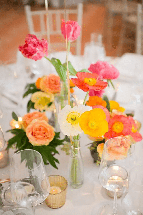 a colorful cluster wedding centerpiece of white, yellow and pink and red poppies, some pink tulips and candles around