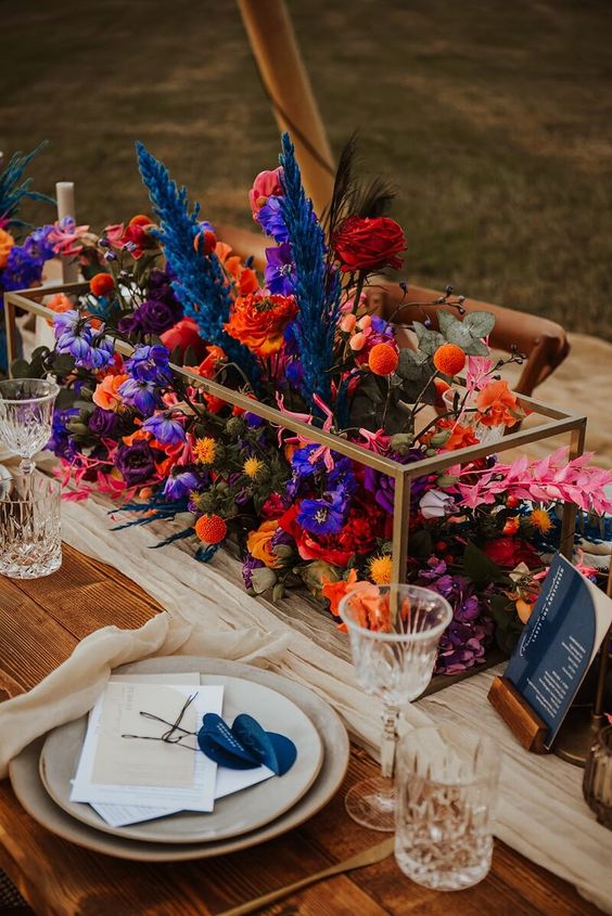 a gorgeous bold wedding centerpiece of a frame filled with violet, navy, orange, red blooms and dried leaves