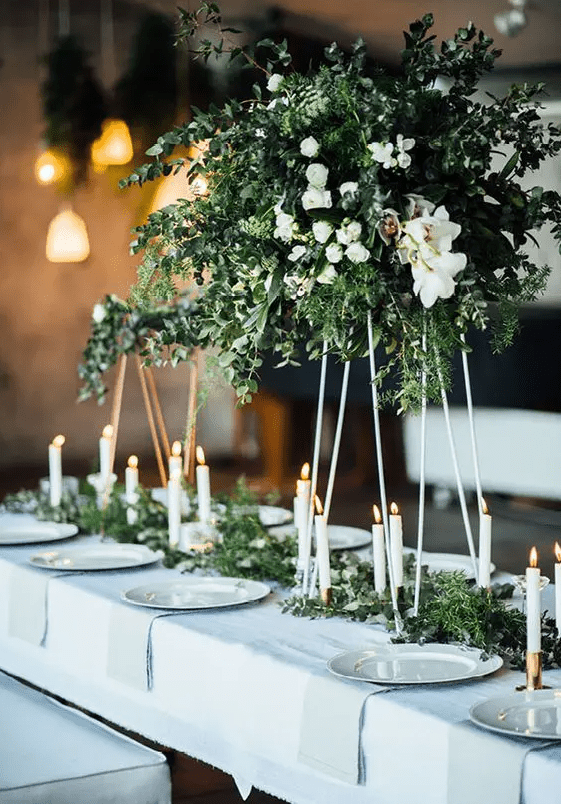 a gorgeous modern centerpiece with lush textural greenery, white blooms on metal stands