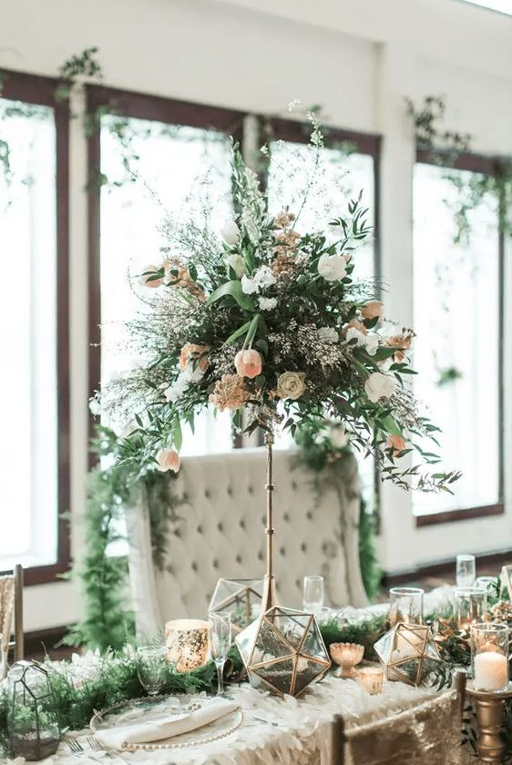 a textural centerpiece of white and blush blooms with textural cascading greneery on a tall brass stand