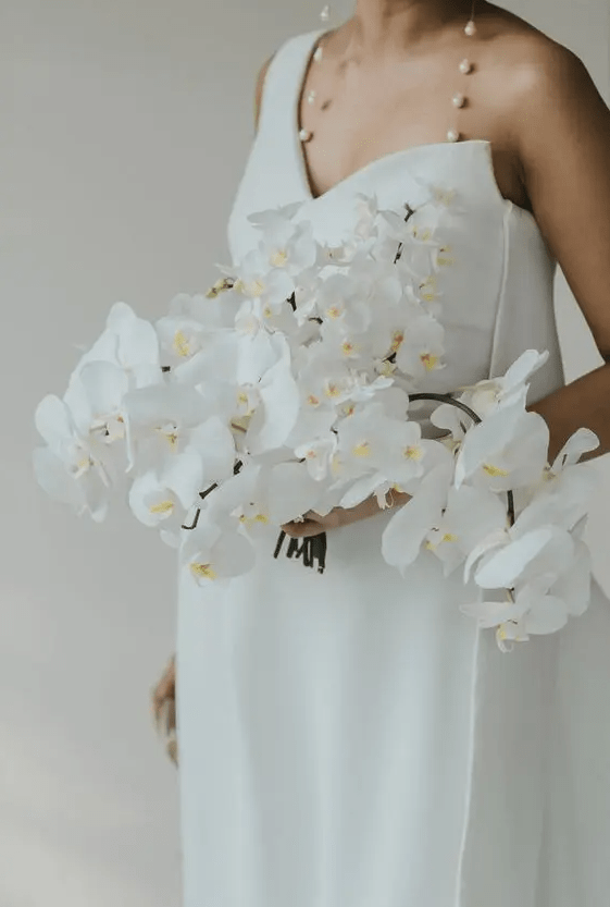 a lush and cascading white orchid wedding bouquet looks jaw-dropping with a minimalist wedding dress and lovely baroque pearl earrings