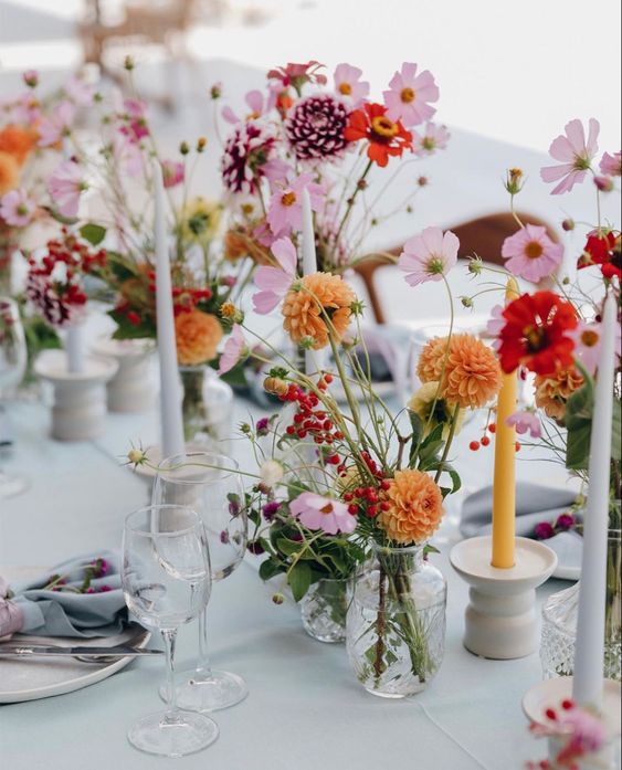 a colorful cluster wedding centerpiece of pink, red, orange and purple blooms and colorful candles