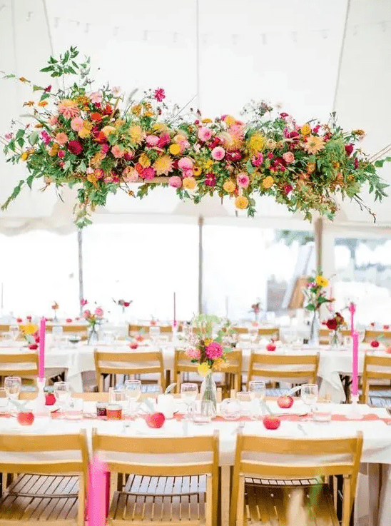 a bright floral wedding installation of yellow, pink, fuchsia blooms and greenery is a very cheerful idea