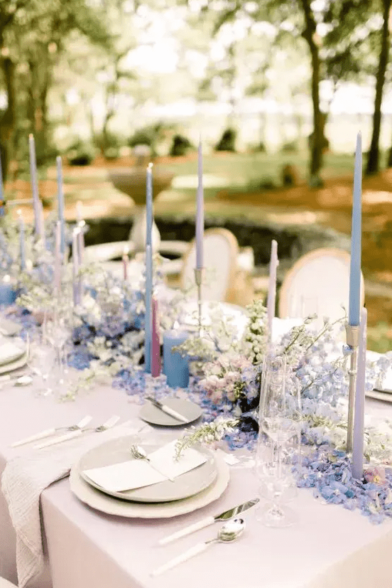 a beautiful and elegant wedding tablescape done in neutrals but with a periwinkle floral runner, blue, lilac and blush thin and tall candles