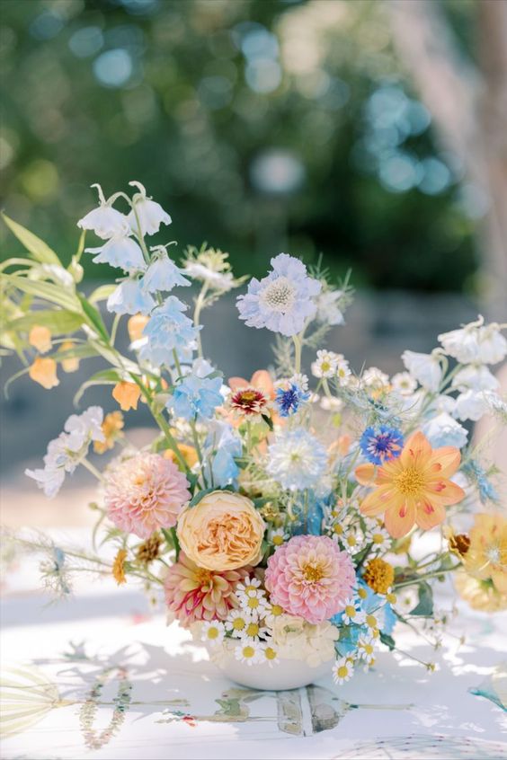 a beautiful summer wedding centerpiece of pastel pink, blue and yellow flowers, greenery and some smaller fillers