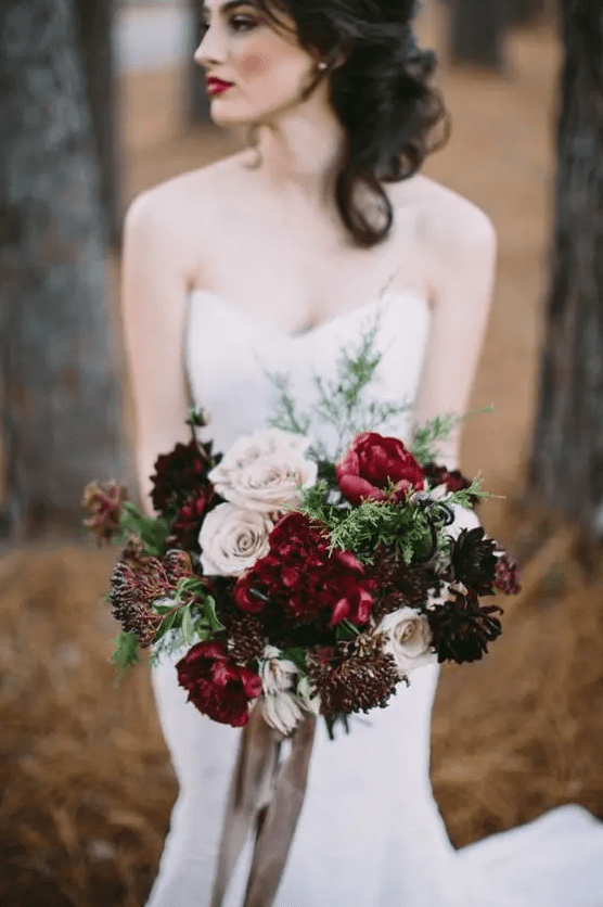 a bold Christmas wedding bouquet of blush, burgundy and deep purple blooms, berries and greenery