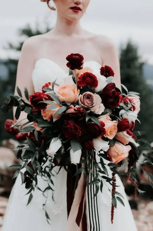a bold Halloween wedding bouquet with burgundy, dusty pink, orange blooms, usual and dark foliage and striped ribbons