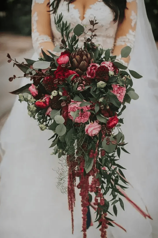 a bold exquisite cascading wedding bouquet of pink, burgundy blooms, greenery, dark foliage, artichokes and bulbs going down for a fall wedding