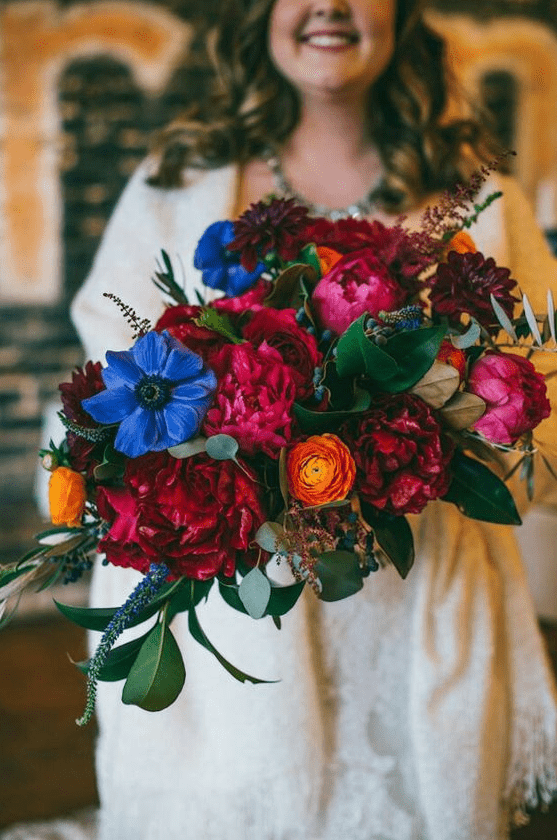 a bold wedding bouquet with fuchsia, red, blue, yellow flowers, privet berries and foliage for a bright fall wedding