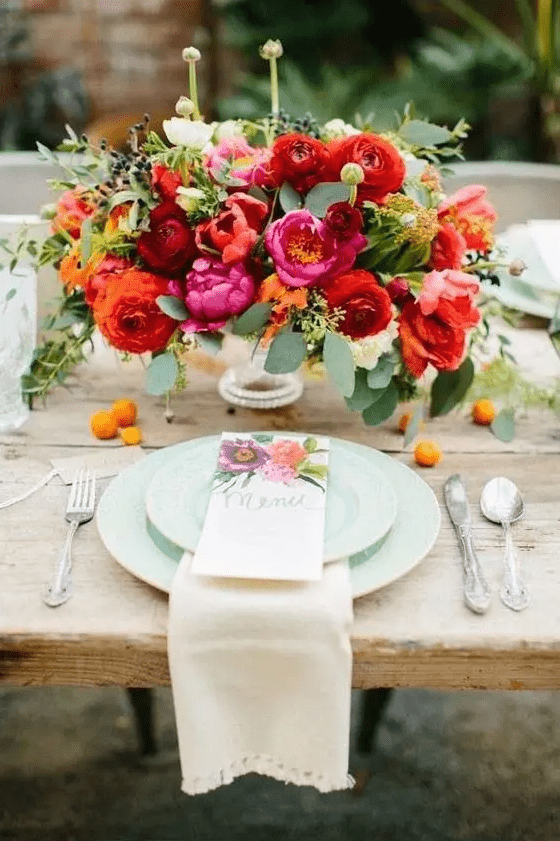 a bright floral centerpiece with pink peonies, parrot tulips, burgundy ranunculus and greenery