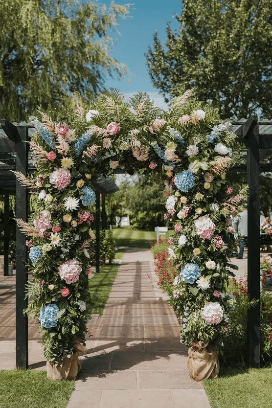 a bright wedding arch with plenty of texture, with greenery, pink and blue hydrangeas, pampas grass and some roses and dahlias