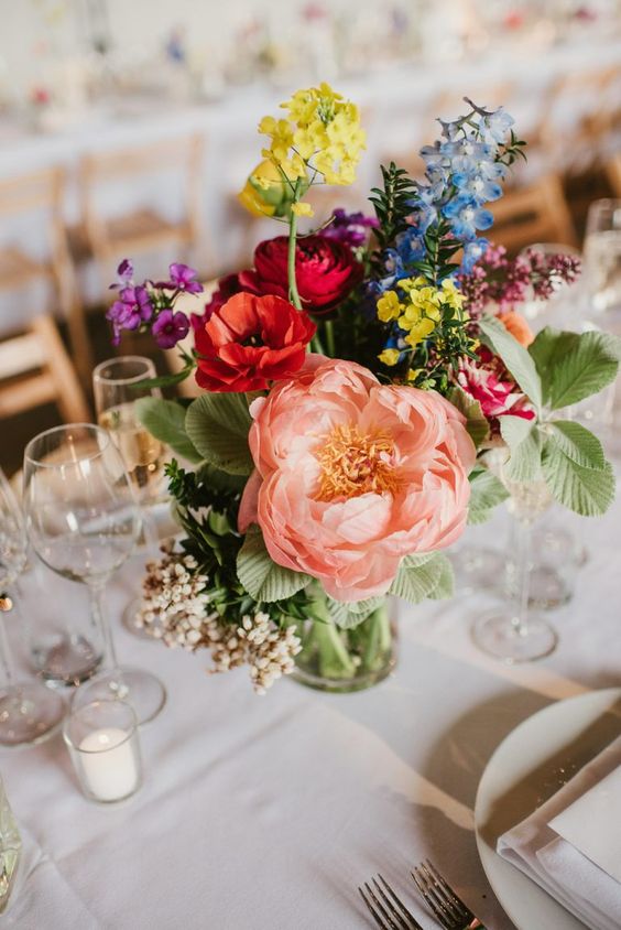 a bright wedding centerpiece of blush, red, yellow, purple and blue flowers and greenery is amazing for summer