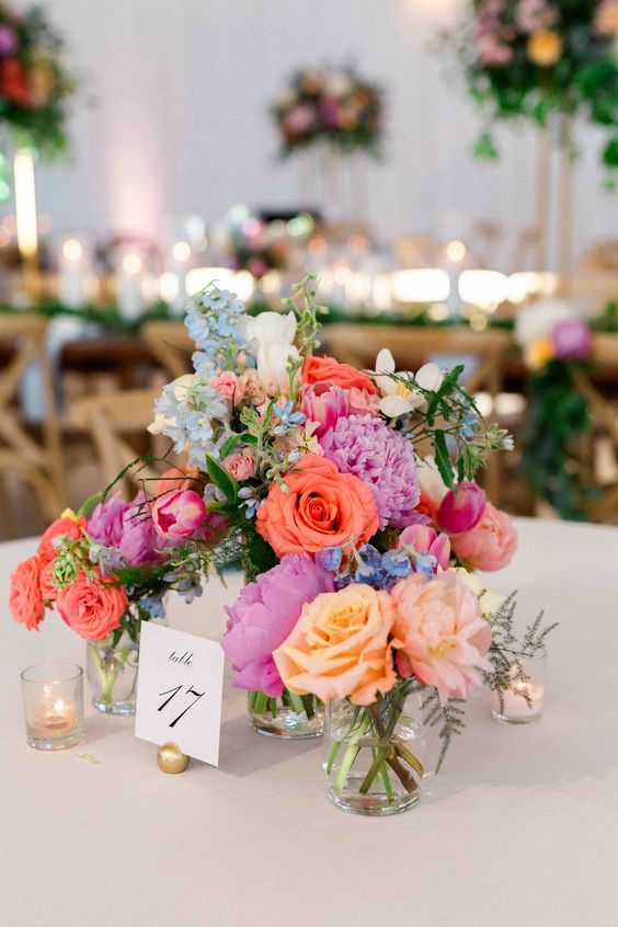 a bright wedding centerpiece of pink, coral, blue and violet blooms and some greenery for summer