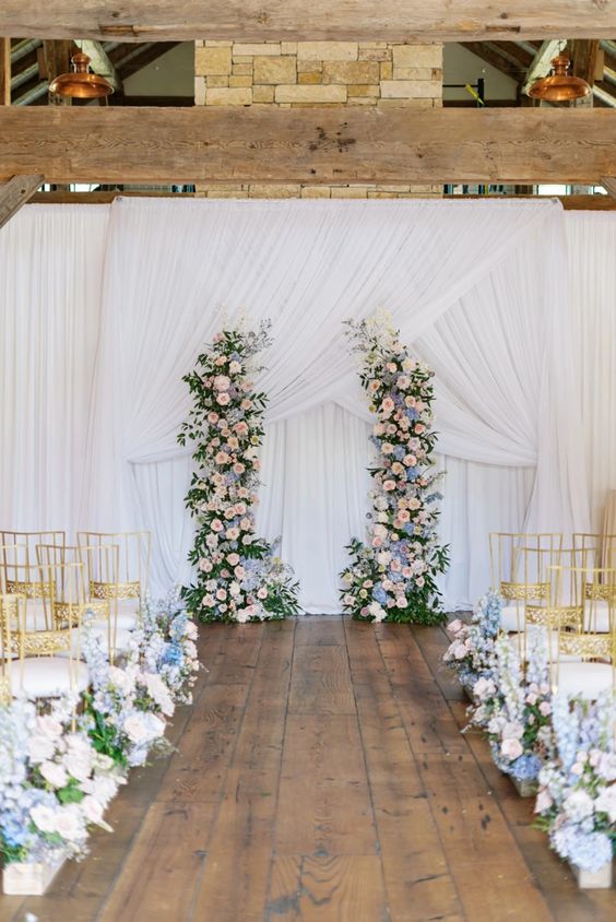 a chic pastel wedding altar with greenery, blush and blue flowers and matching arrangements along the aisle