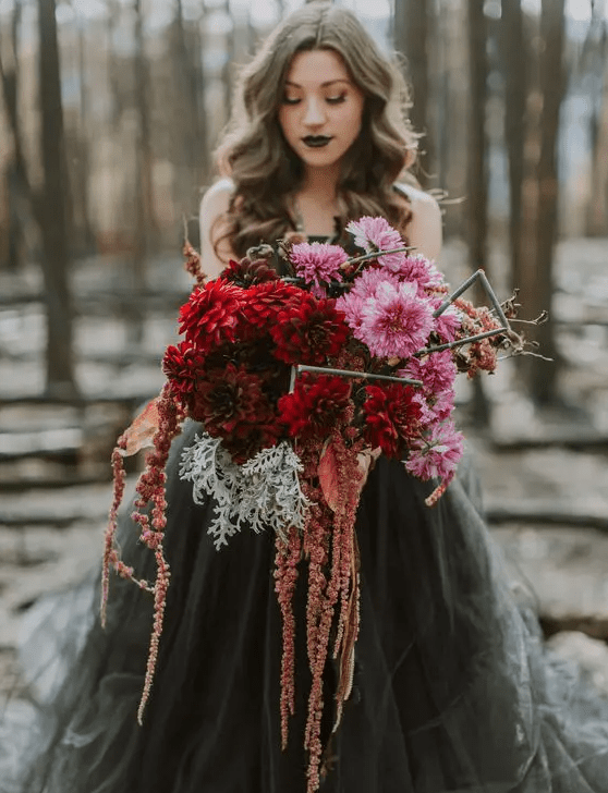 a colorful and textural wedding bouquet of pink, red and rust cascading blooms, pale millet and stems to stand out with a black wedding dress