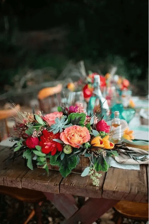 a colorful box centerpiece with orange, red, pink and yellow blooms, herbs and succulents