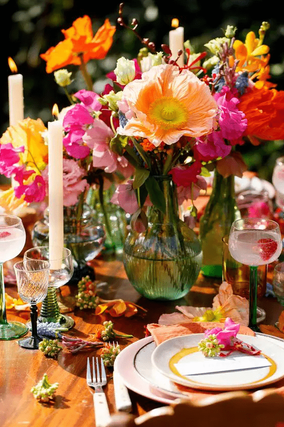 a colorful summer wedding centerpiece of orange and yellow poppies, pink, fuchsia, blue and hot pink blooms and candles for a festival wedding