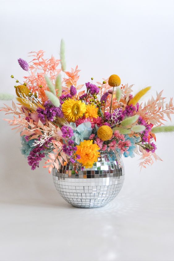 a colorful wedding centerpiece of a disco ball, purple, marigold, blush blooms and dried leaves
