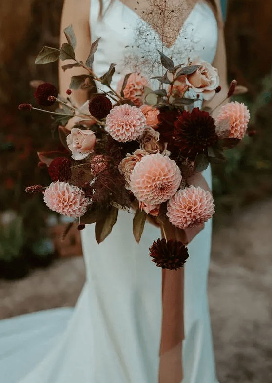 a contrasting fall wedding bouquet of burgundy and pink dahlias, berries, greenery and long ribbon is a lovely idea