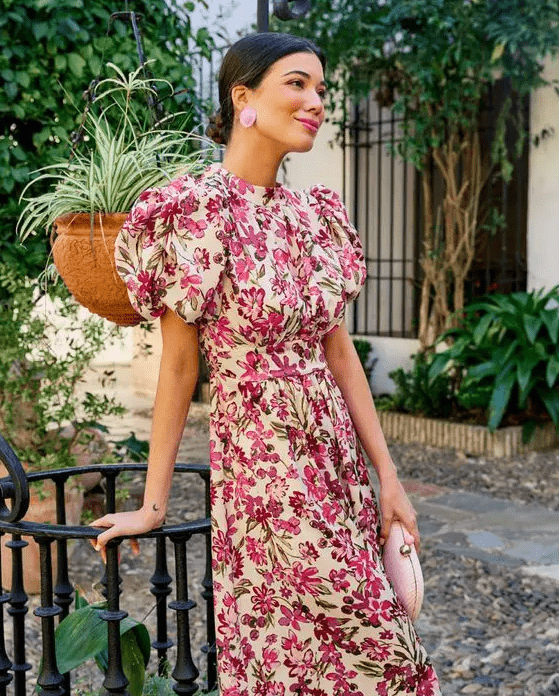 a cute guest look with a bright floral dress with puff sleeves, pink earrings and a pink clutch is cool