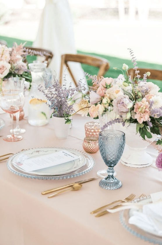a cute pastel wedding tablescape with pink linens, pink, white blooms and lavender, blue and pink glasses
