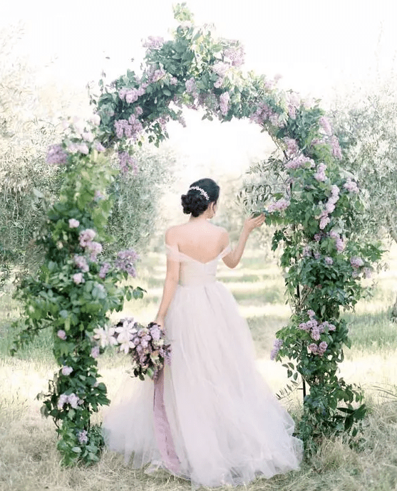a dreamy garden wedding arch with greenery and lilac is a chic idea that looks incredibly romantic and very beautiful