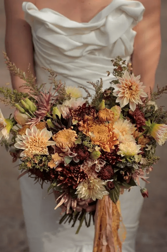 a fall wedding bouquet of blush, rust and burgundy dahlias, chrysanthemums, greenery and herbs, some ribbons