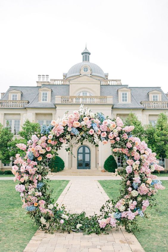 a gorgeous round pastel wedding arch styled with greenery, blush and blue roses and hydrangeas looks magical