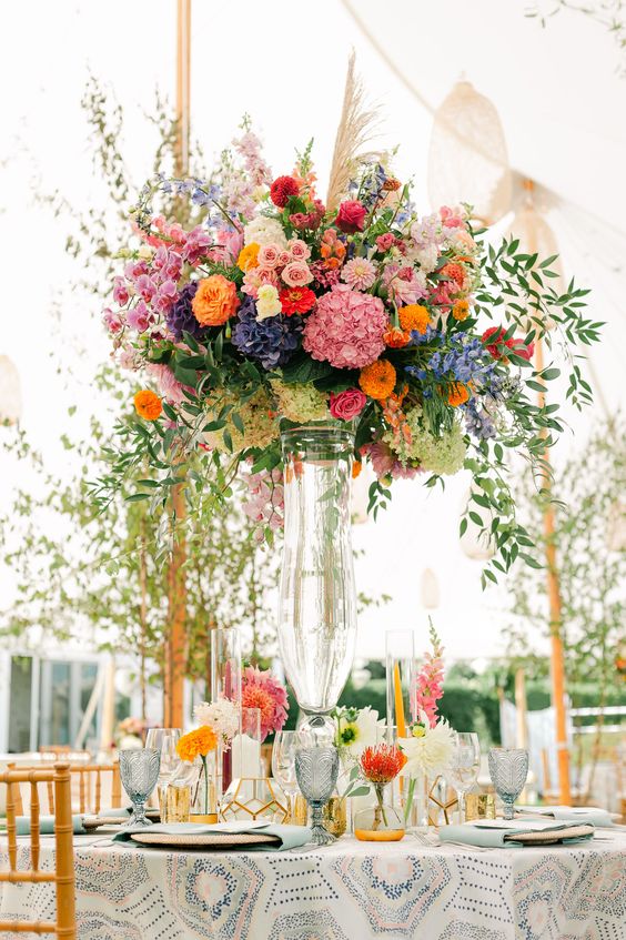 a gorgeous tall wedding centerpiece of blush, pink, orange, violet and blue flowers and greenery for a summer wedding