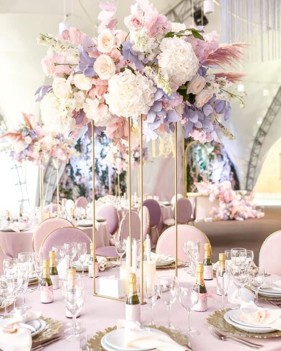 a gorgeous tall wedding centerpiece on gold stands, with blush, neutral and lilac blooms, pink pampas grass and white blooming branches