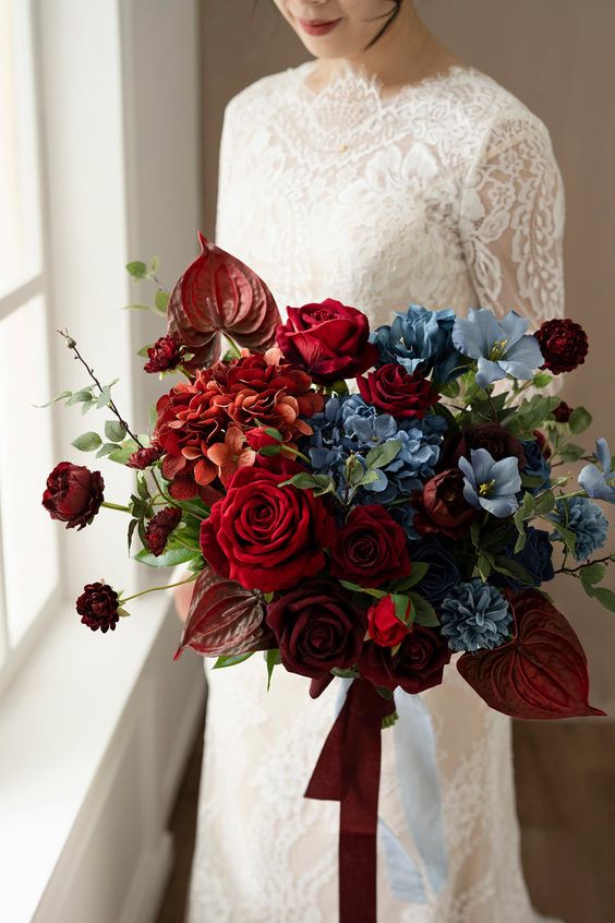 A jaw dropping burgundy and blue wedding bouquet with roses, hydrangeas, greenery and twigs is wow