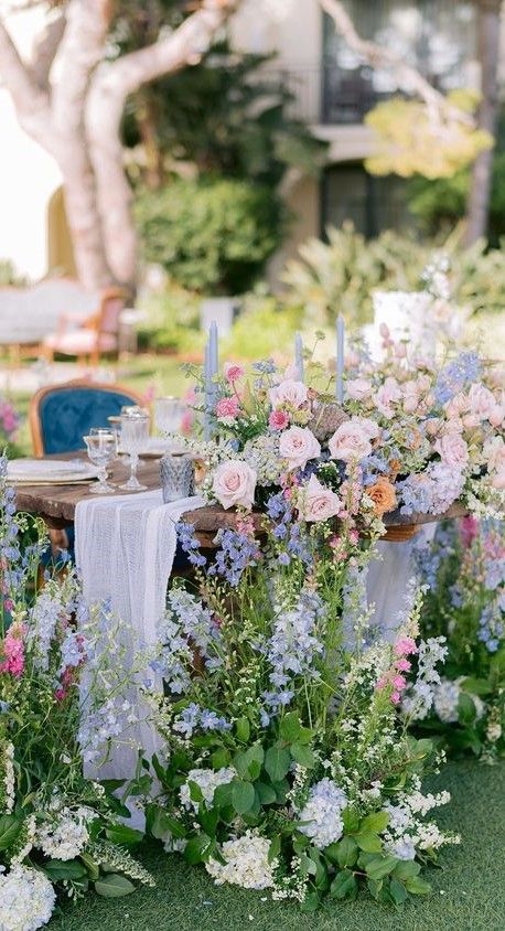 a lovely and lush pastel wedding centerpiece of blush, blue and pink blooms dotted with blue candles is amazing