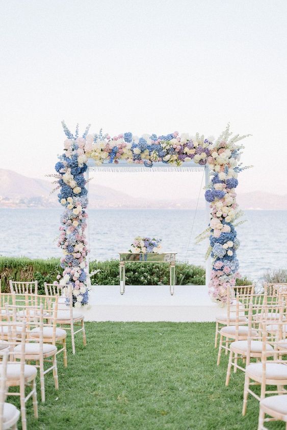 a lovely and textured wedding arch done with delphinium, hydrangeas and roses in blush, blue and periwinkle plus a sea view
