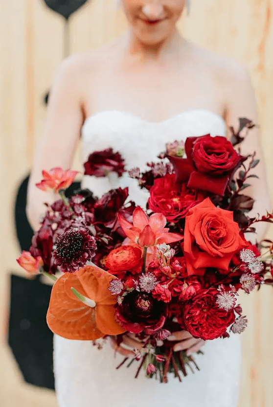 a lovely modern wedding bouquet with deep red, burgundy and purple blooms, an orange piece is wow