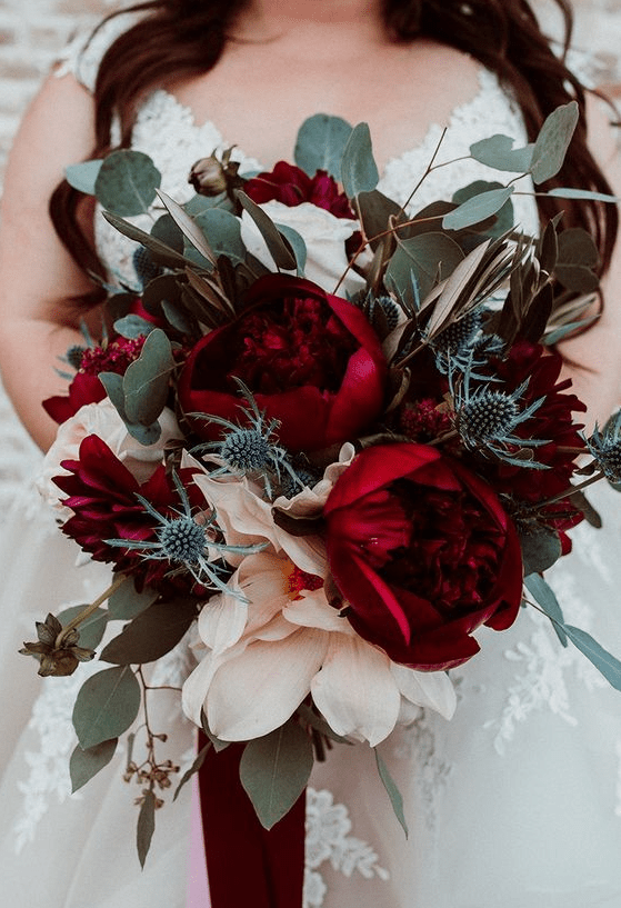 A lush and bol fall wedding bouquet of oversized deep red peonies, greenery and thistles is just jaw dropping
