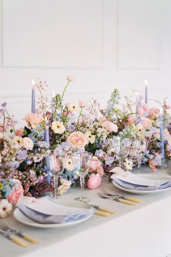a lush wedding table centerpiece of blush, neutral and periwinkle blooms, greenery and periwinkle candles