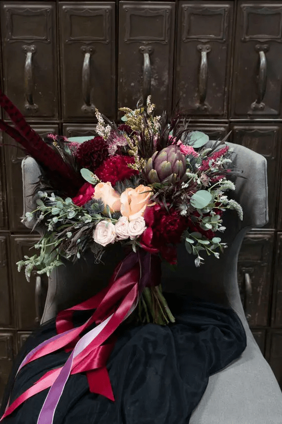 a luxurious wedding bouquet with feathers, artichokes, thistles, eucalyptus, deep red and burgundy blooms
