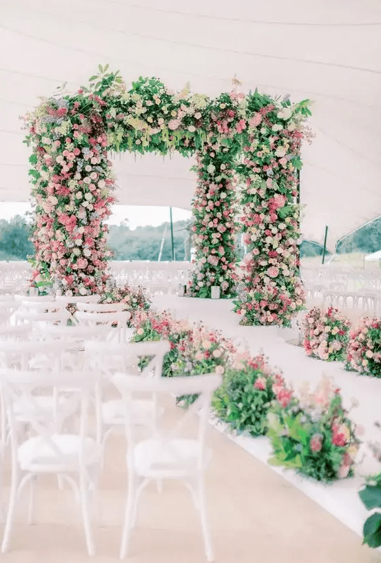 a massive wedding arbor covered with greenery, pink, lilac, blush and white blooms plus a matching wedding aisle