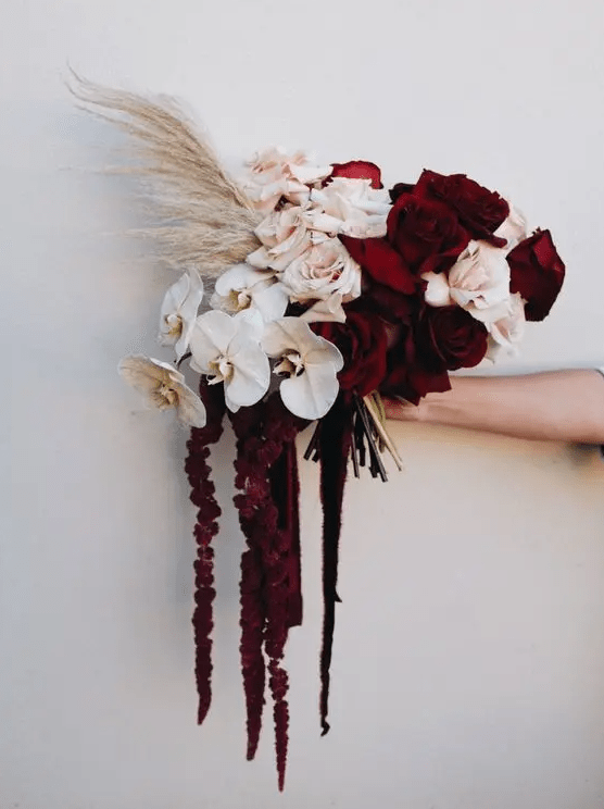 a moody wedding bouquet of burgundy and blush roses, white orchids, pampas grass, amaranthus is a chic and refined wedding idea