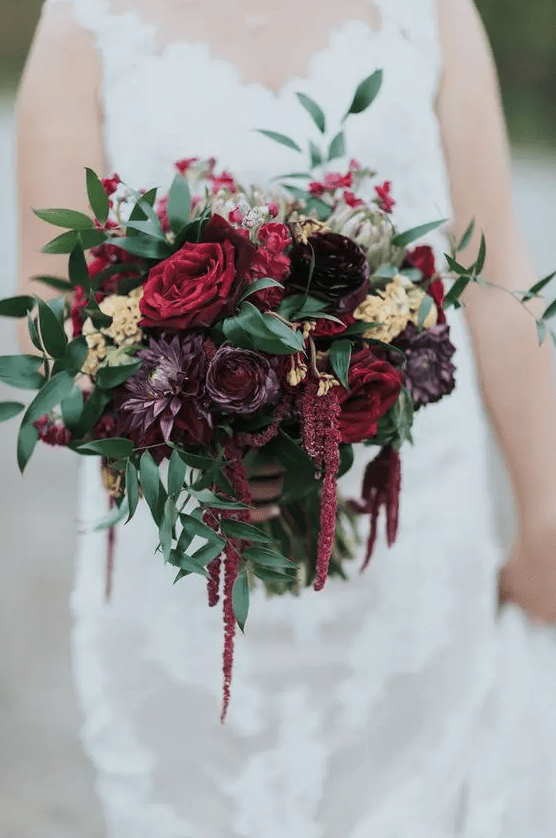 a moody wedding bouquet of burgundy roses, purple ranunculus and dahlias, greenery and amaranthus is amazing for the fall