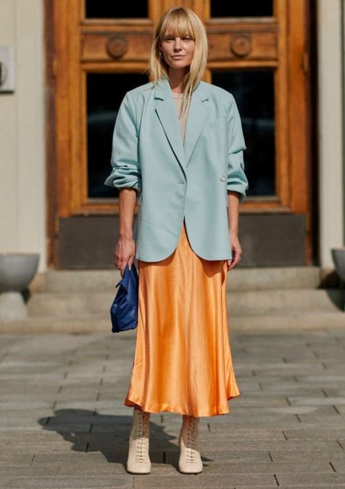 a neutral top, an orange slip midi skirt, a light blue oversized blazer, nude boots and a navy bag for a trendy modern look at the shower