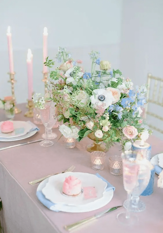 a pastel spring wedding table in pink and blue, with pink and blue candles, blue napkins and a pink tablecloth, blush florals and candles