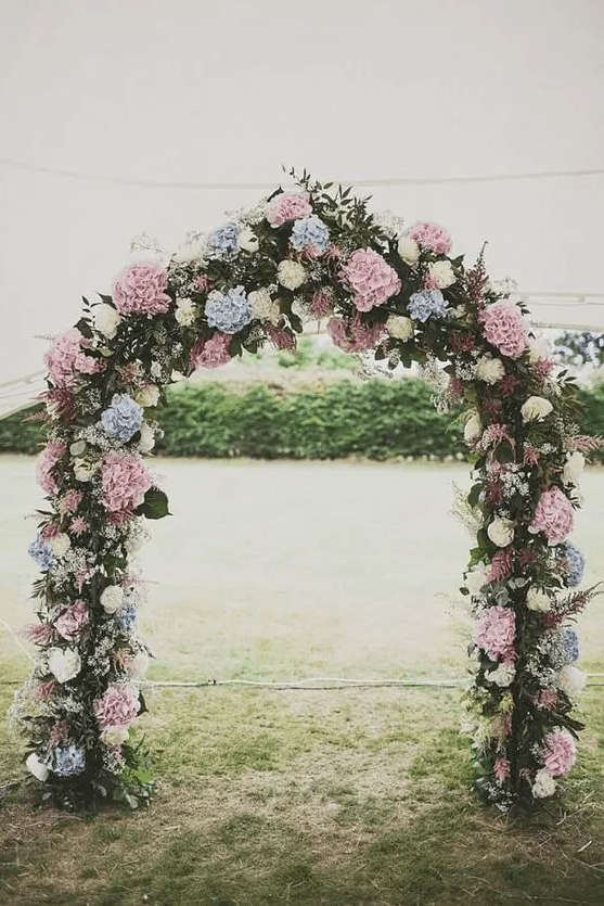 a pastel wedding arch with plenty of foliage and greenery, white, pink, blue hydrangeas is a cool and budget-friendly solution