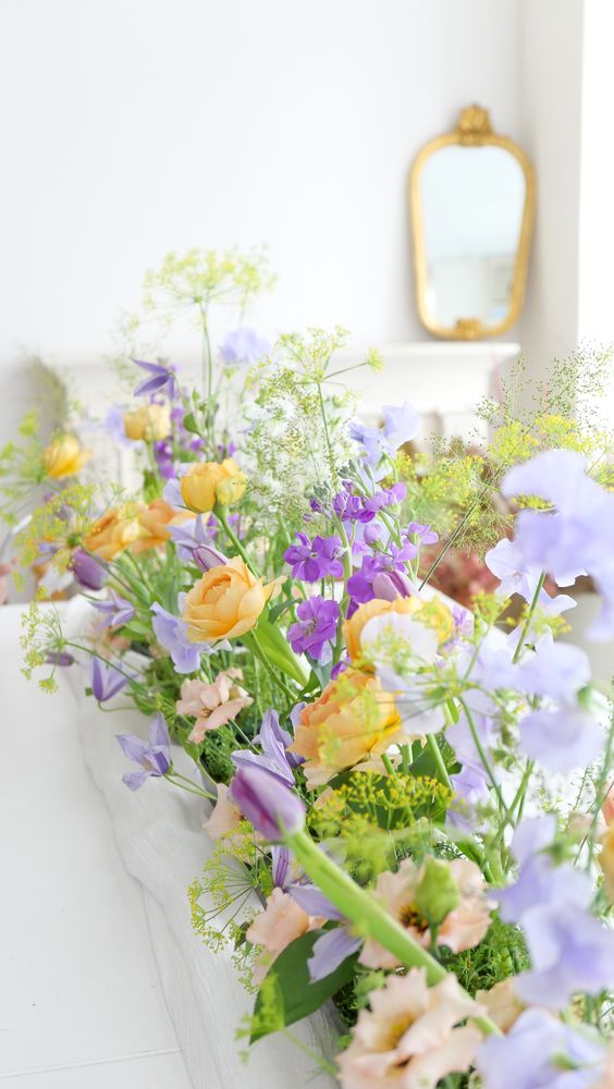 a pastel wedding centerpiece of lilac, periwinkle, orange blooms and greenery is a cool idea for spring
