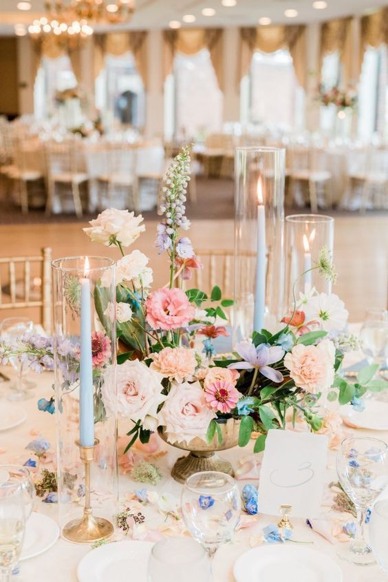 a pastel wedding centerpiece of peachy, blush and blue blooms and blue candles is amazing for a sprign wedding