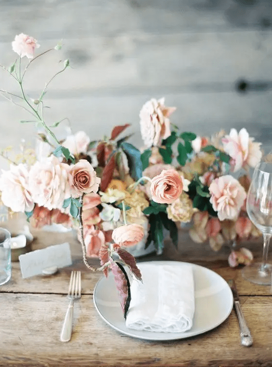 A pastel wedding centerpiece with blush and light colored mauve blooms with greenery